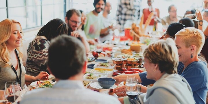 A diverse group of people enjoying a vibrant dinner party. This lively gathering features men and women of various ethnicities sharing food, laughter, and conversation around a beautifully set table.