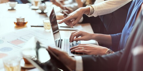 Group of professionals collaborating at a desk with laptops and documents. Hands pointing at screens, teamwork in a business meeting, team working together. Business people in a boardroom meeting.