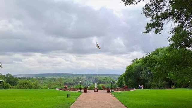 The Zimbabwean flag waves proudly atop the Victoria Falls Hotel flagpost, framed by the iconic Victoria Falls Bridge and the misty gorge of the Zambezi River below.