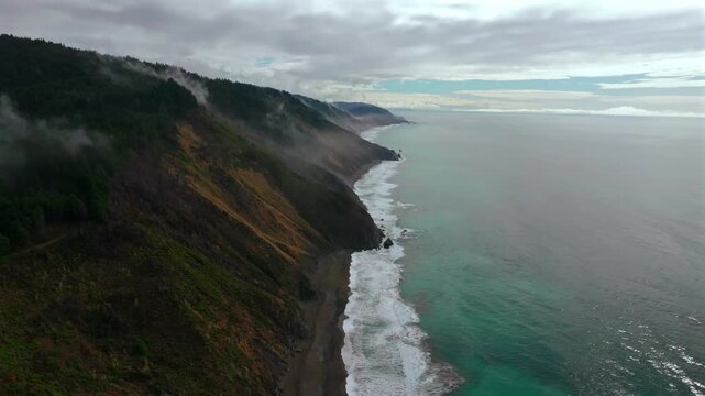 Rugged remote untouched black sand beach USAL Beach Sinkyone Wilderness Northern California aerial drone waves crashing mist fog rain coastline bluffs Lost Coast Trail forward down motion
