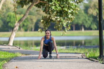 Young asian sportswoman smiling and preparing for a run in a park by a serene lake, wearing a...
