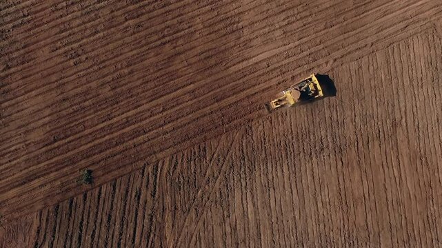 Aerial rises over diagonal pattern as bulldozer levels sandy soil