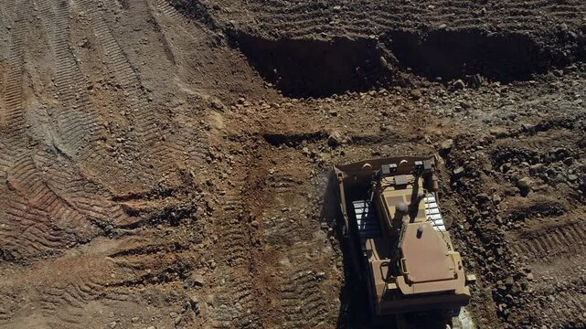 High angle: Heavy industrial bulldozer levels ground, pushing gravel