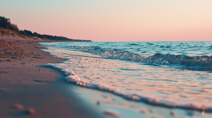 Soft pink and orange hues fill the sky as the sun sets over the calm ocean. Gentle waves create a soothing rhythm along the sandy beach, enhancing the peaceful atmosphere