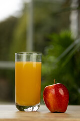 A glass of multifruit juice and an apple on the table by the window. Apple