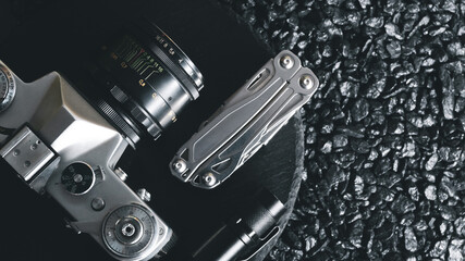 Fototapeta premium Multifunctional tool in folded position lies with retro camera on dark stone background