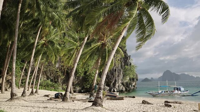 View of palm trees and an anchored boat at 7 Commandos Beach during a stunning sunset, with golden hues reflecting on the tranquil water.
