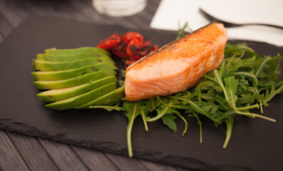 Baked sea trout fillet with fresh vegetables and herbs on black board