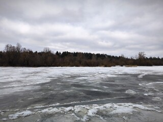 Snow-covered blocks of ice on the river above the gray overcast sky. Frozen water surface on the...