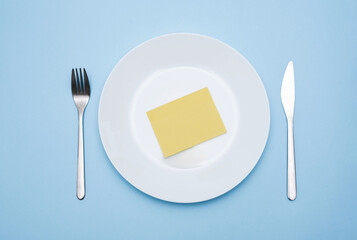 White plate with yellow note and cutlery on blue background, dieting concept