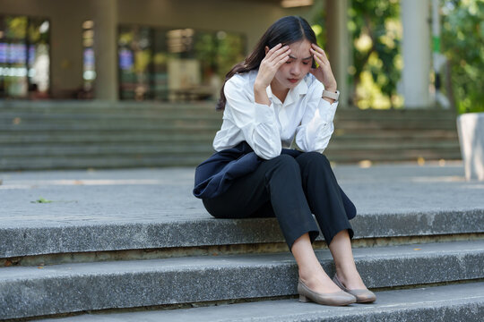 Young businesswoman sitting on steps, holding her head in frustration. She appears overwhelmed, possibly facing work-related stress or personal challenges in a public urban setting