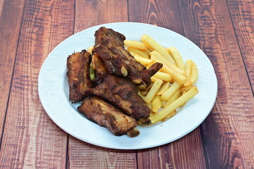 A plate of ribs and french fries sits on a wooden table