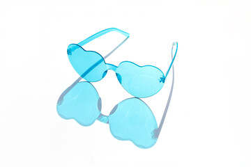 a pair of blue-tinted sunglasses with heart-shaped lenses. The sunglasses are placed on a white surface, and their reflection is visible below them.