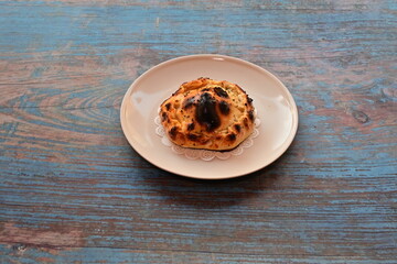 A burnt pastry sits on a white plate on a wooden table