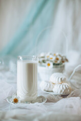 A glass of fresh milk is placed on a decorative plate alongside white pastries, with a background featuring soft drapes and a floral arrangement, creating a calm atmosphere