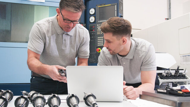 Male Engineer And Apprentice Checking Components Whilst Looking At Laptop