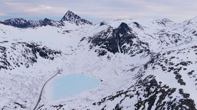 Aerial shot of a frozen lake surrounded by snowy mountains in Norway's winter landscape