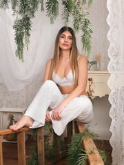 Fototapeta premium Woman in White Attire Poses Elegantly in a Beautifully Decorated Indoor Space With Greenery and Vintage Furniture