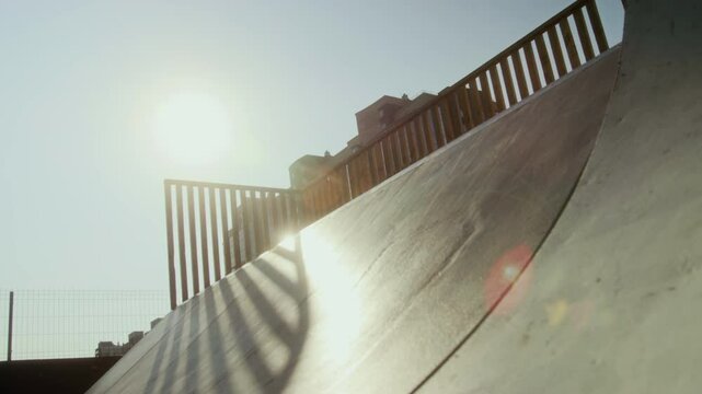 Low angle view of BMX athlete balancing on front wheel of bike while practicing nose pick trick on skate park ramp on sunny summer day