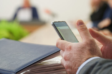 Business communication on smartphone. Businessman using a smartphone during a meeting, symbolizing digital work, multitasking, and corporate communication in a office. Photo. Selective focusing