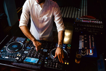 A DJ in a stylish white shirt performs at a nightclub, mixing tracks on professional DJ equipment....