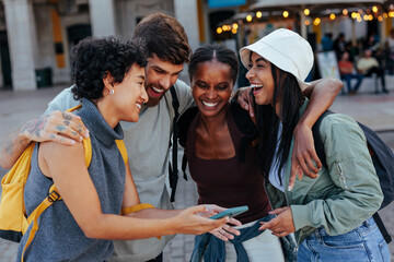 Group of diverse friends laughing together while looking at smart phone