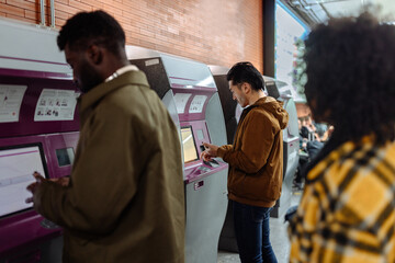 Passengers purchasing train tickets at self-service kiosk in subway station