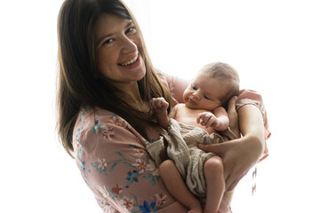 Happy Mothers day! Stylish Mother holding and hugging cute newborn baby in window light, close up....