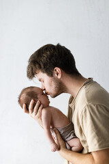 Happy Fathers day!  Stylish father kissing and hugging cute little baby son close up against white wall. Fatherhood and parenthood. Adoption and fertility concept