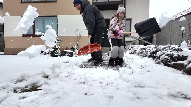 Happy dad and daughter clearing snow near house in winter outside