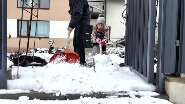 Happy dad and daughter clearing snow near house in winter outside