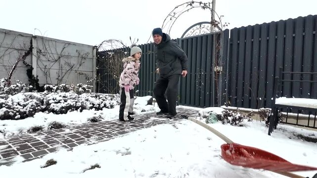 Happy dad and daughter clearing snow near house in winter outside