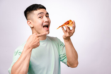 An Asian man in a light green shirt is about to take a bite of a pepperoni pizza slice. He looks...