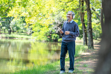 senior man with grey hair wears headsets and holding smartphone,happy in the moment that listening music and dancing in nature