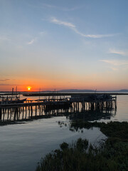 Wooden pier extending over calm water at sunset. The sky transitions from deep blue to warm orange hues.