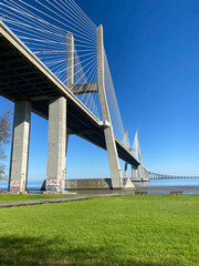 Vasco da Gama Bridge in Lisbon, Portugal, viewed from a green riverside park.
