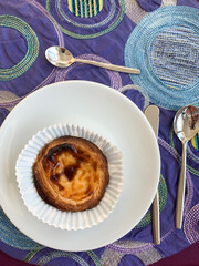 Portuguese pastel de nata custard tart with caramelized top in a white paper cup on a plate.