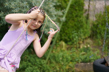 A little cute smiling and positive girl in glasses and a dress with colorful small braids is...
