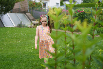 A little cute girl in a dress with small multicolored braids, missing a front tooth, in a summer...