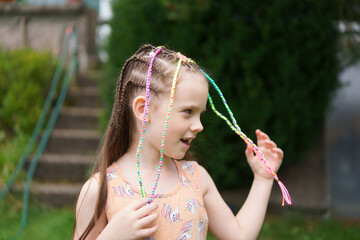 A little cute girl in a dress with small multicolored braids, missing a front tooth, in a summer...
