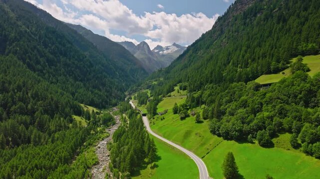 A breathtaking aerial view of the picturesque landscape surrounding Simplon, Switzerland in summer, showcasing lush green valleys, rugged mountain peaks, and winding roads under clear blue skies.
