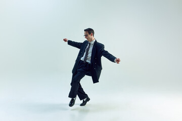 Young businessman moving with open arms and playful energy against white studio background. Concept of business, psychology, self-expression, overworked, work-life balance.