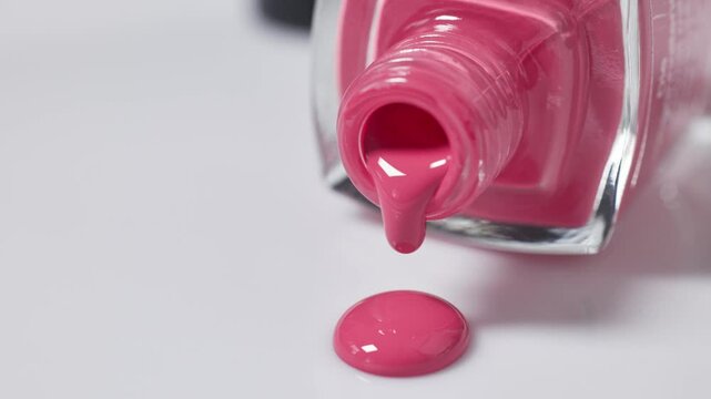 charming pink nail polish slowly dripping from a bottle onto a white surface, cosmetic close-up macro
