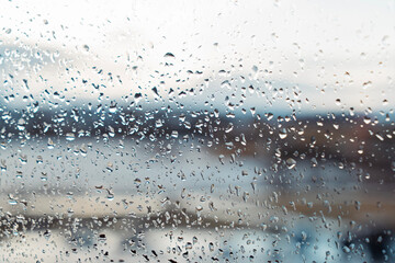 Closeup of raindrops on a window with a blurred, cool-toned misty landscape in the background. The droplets add texture and depth to the serene rainy day mood