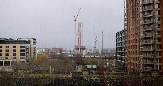 Footage of construction work being done on a new block of apartments located in the Leeds City Centre in the UK showing cranes and the new apartment block on a cold rainy day in the winter