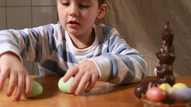 Cute little Boy with bunny ears plays with colored painted eggs, closes eyes with toy, plays hide and seek. Egg hunt, traditional catholic orthodox easter.  Little boy celebrate Easter at home