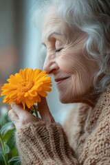 A senior woman smiles gently while holding a vibrant orange flower close to her face, showcasing a moment of joy and tranquility