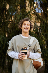 Fototapeta premium Stylish young man enjoying a coffee while standing among lush greenery in a vibrant urban setting
