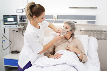 A nurse provides care to an elderly woman using a breathing mask in a medical clinic environment