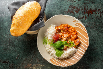 A delicious serving of rice accompanied by rich, creamy curry, garnished with saffron and fresh herbs, with a crispy bread in the background, creating an appetizing meal scene.